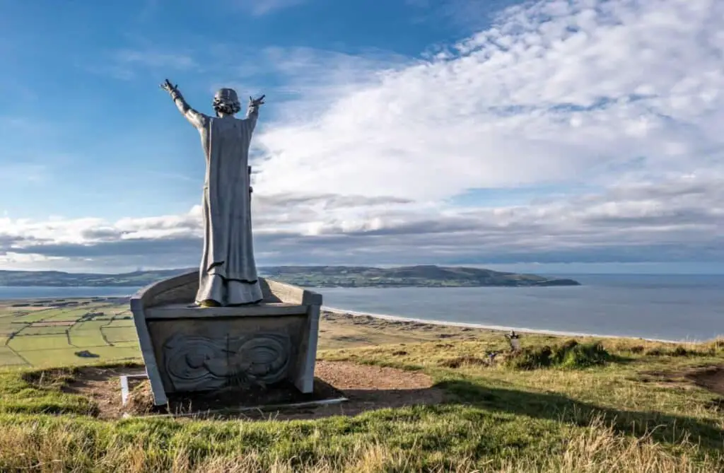 a statue of a man with his arms out on top of a hill overlooking a body of water