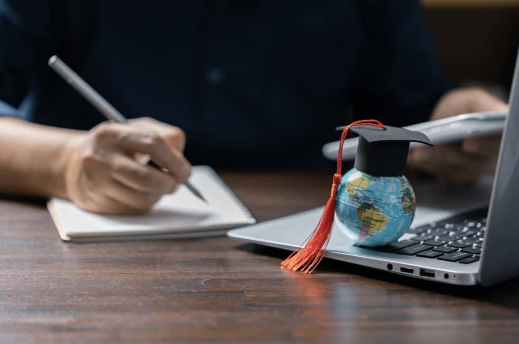 a hand holding a pen and a small globe on a laptop